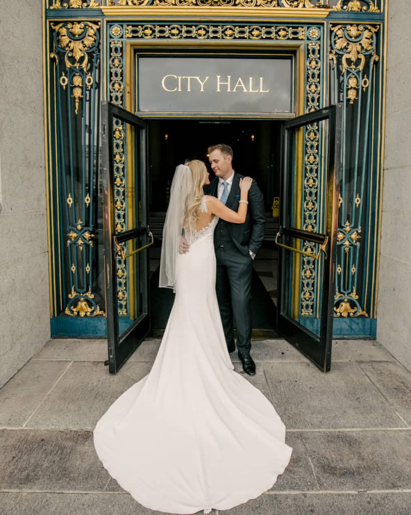 a bride with a long train posing in front of the main sf city hall entry