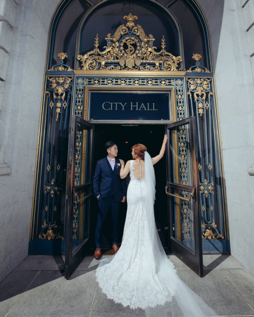 a bride with a long train posing at the main door at city hall